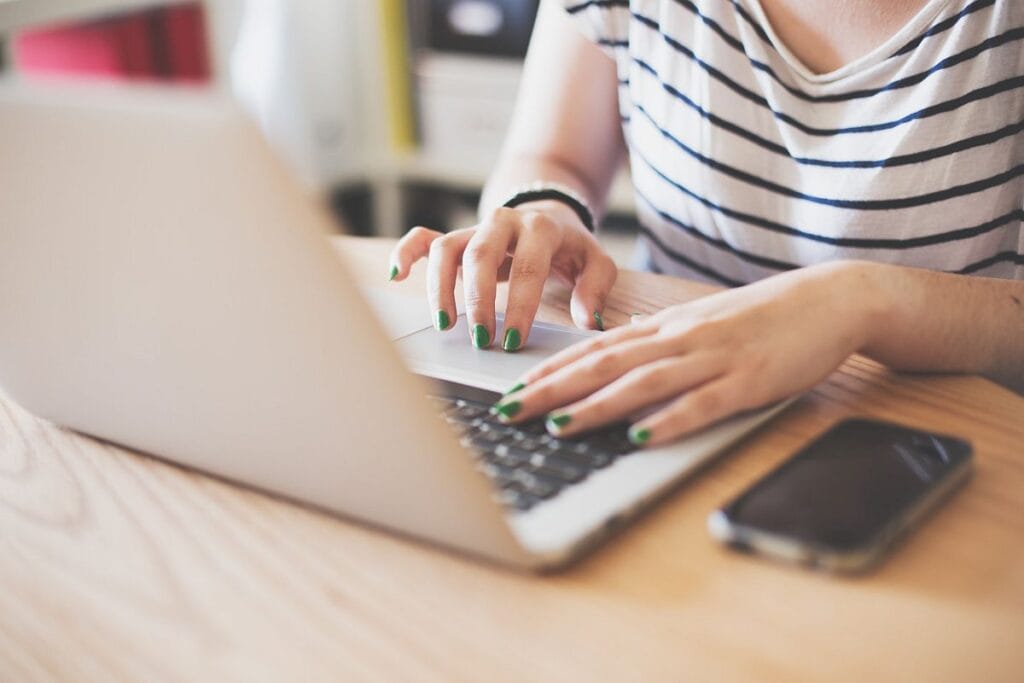 closeup of woman's hands typing on a silver laptop; patient hub enrollment concept