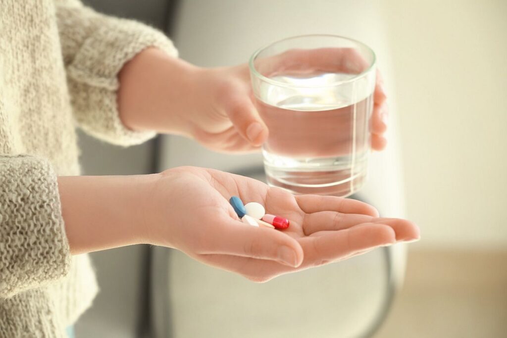 Close up of female holding several pills in one hand and glass of water in the other; adherence challenges concept