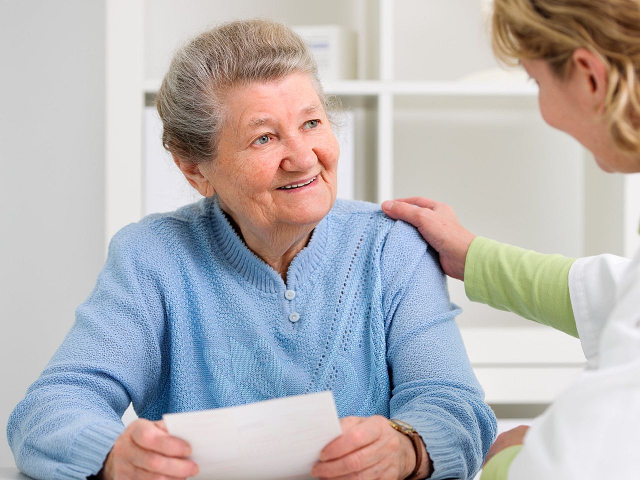 Healthcare professional puts hand on should of smiling older lady; patient care coordinators concept