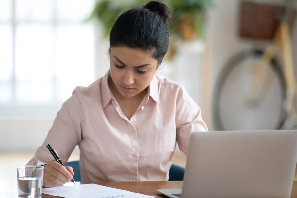 Seated woman making notes on paper, with laptop open; value of rare disease therapies concept