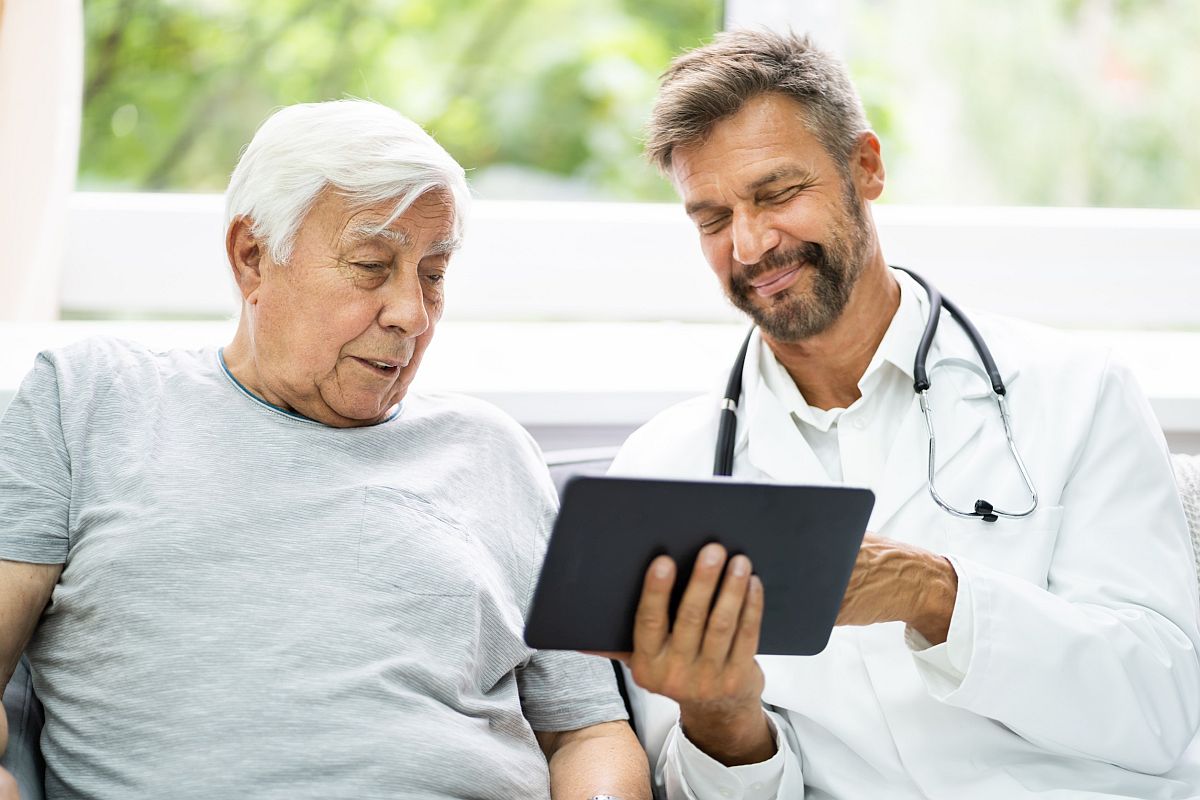 Older man looking at tablet shown to him by a smiling healthcare professional; uninsured patients concept