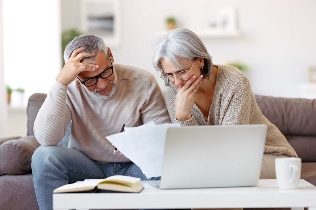 Older couple looking at papers with laptop open; uninsured patients concept