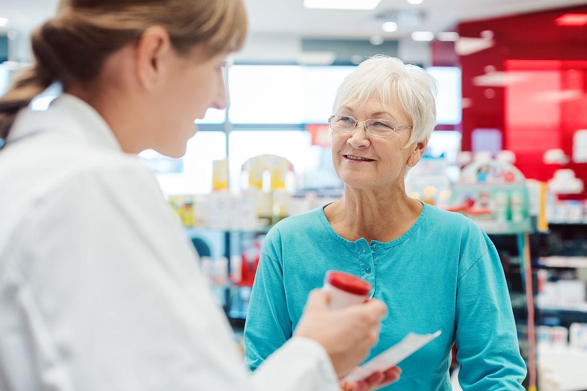 Healthcare worker in pharmacy serves woman; specialty drug access concept