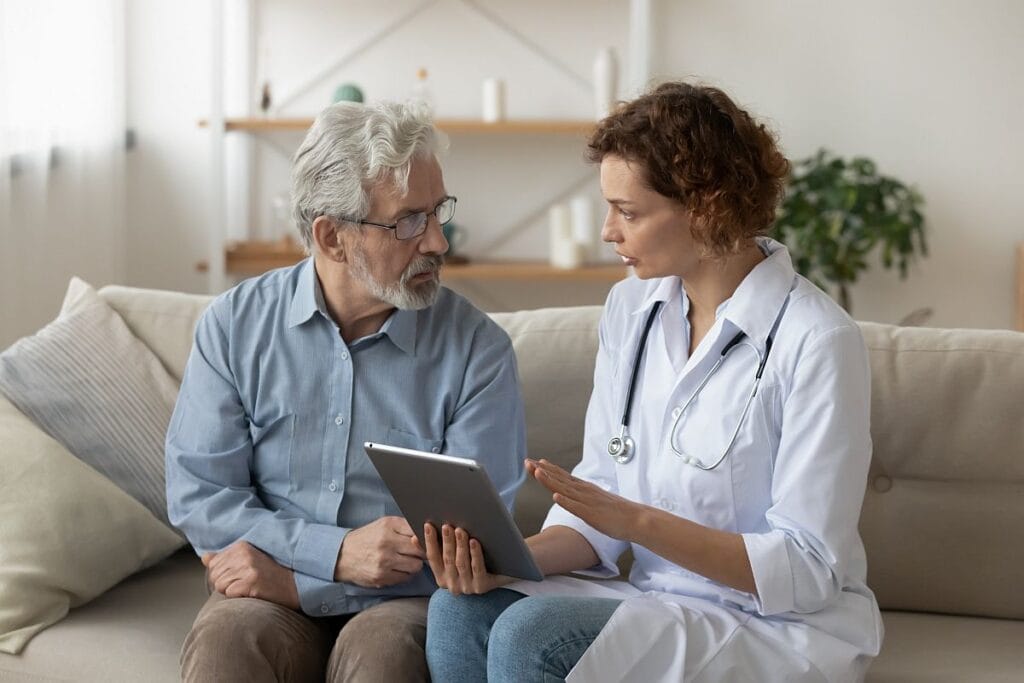 Healthcare professional sitting with older male patient, explaining something; patient nonadherence concept