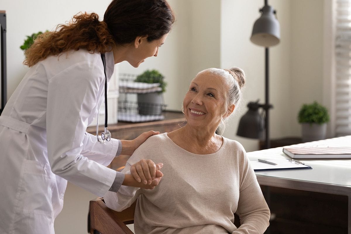 Medical worker in white coat with stethoscope holding older woman's hand; demonstrate value concept