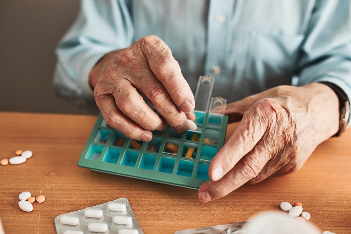 Senior person organizing medication into a pill dispenser; patient nonadherence concept.