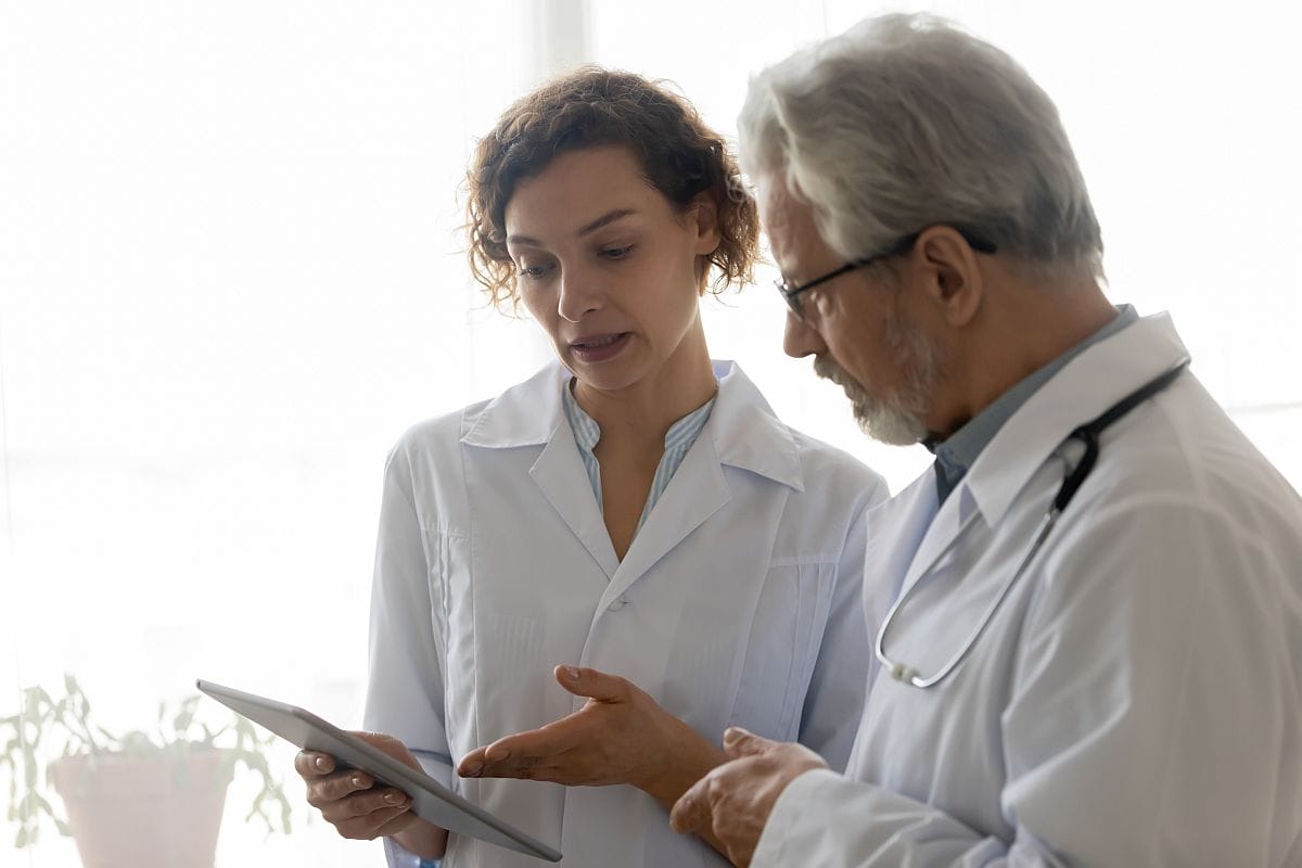 Medical practitioners in discussion, looking at information on a tablet; nonadherence concept