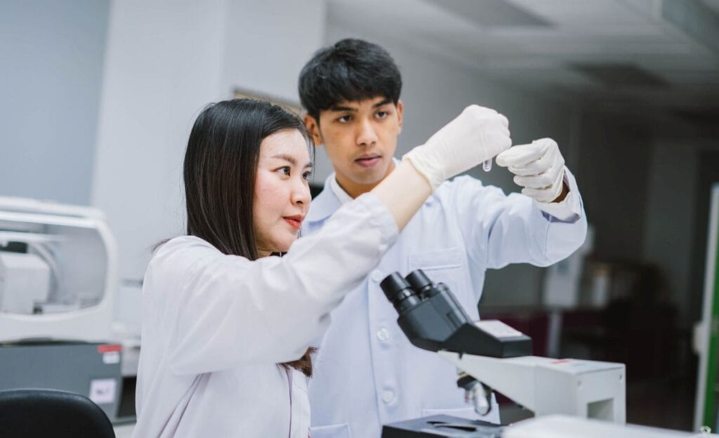 Two techs in lab examining test tube; expanded genetic testing concept