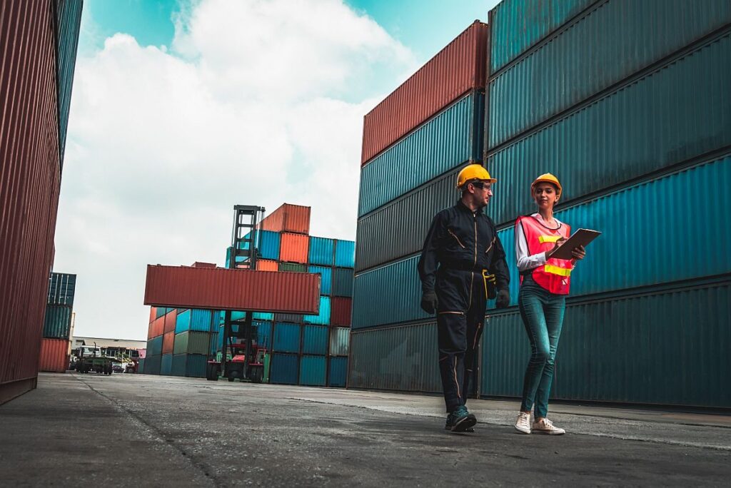 Workers walking next to stacks of shipping containers; pharmaceutical supply chain concept