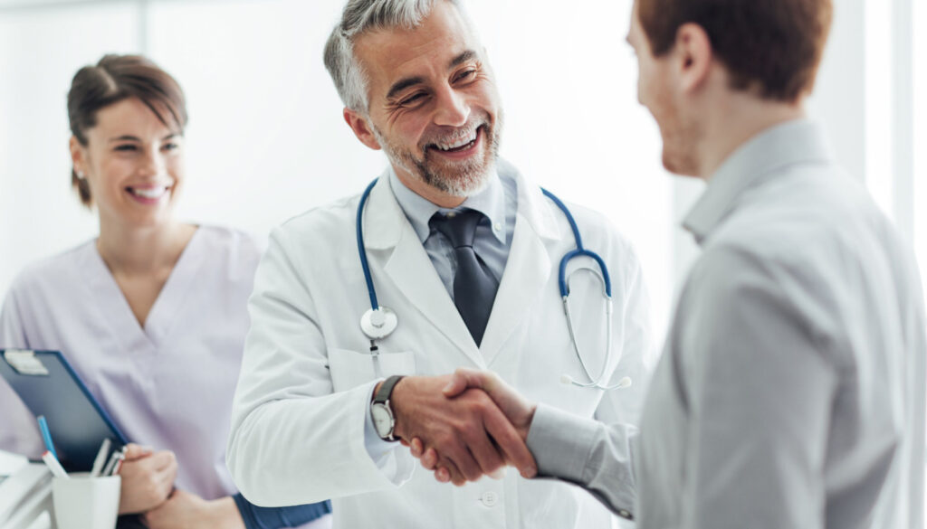 Doctor shaking man's hand, with healthcare worker looking on; collaborative patient management concept