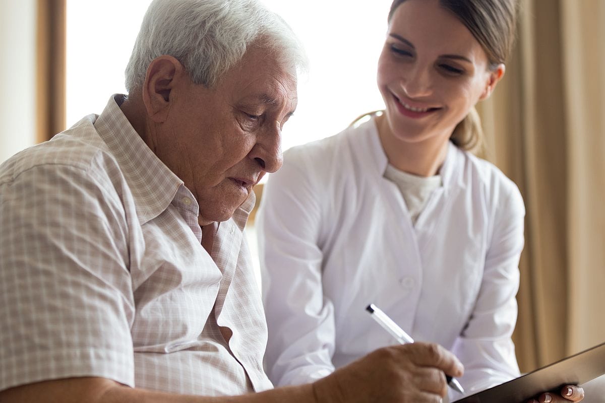 Smiling young female doctor visit senior male; financial assistance rare disease concept