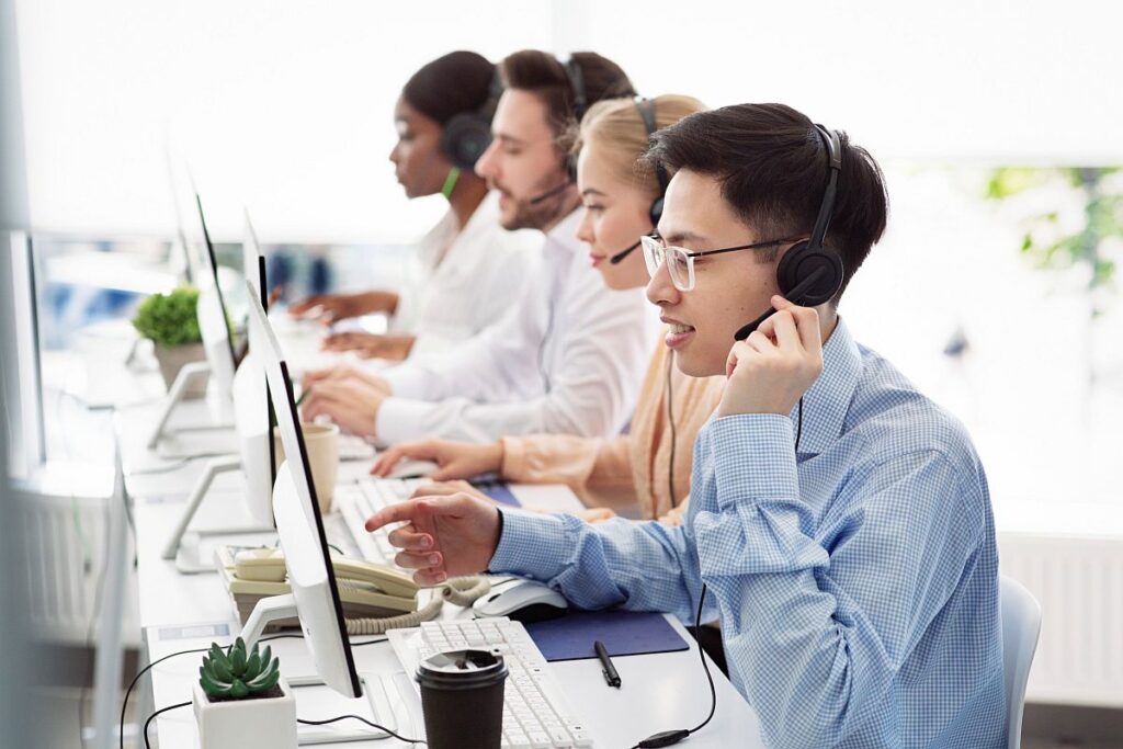 Row of call workers using headsets and sitting in front of computers; specialty therapies concept