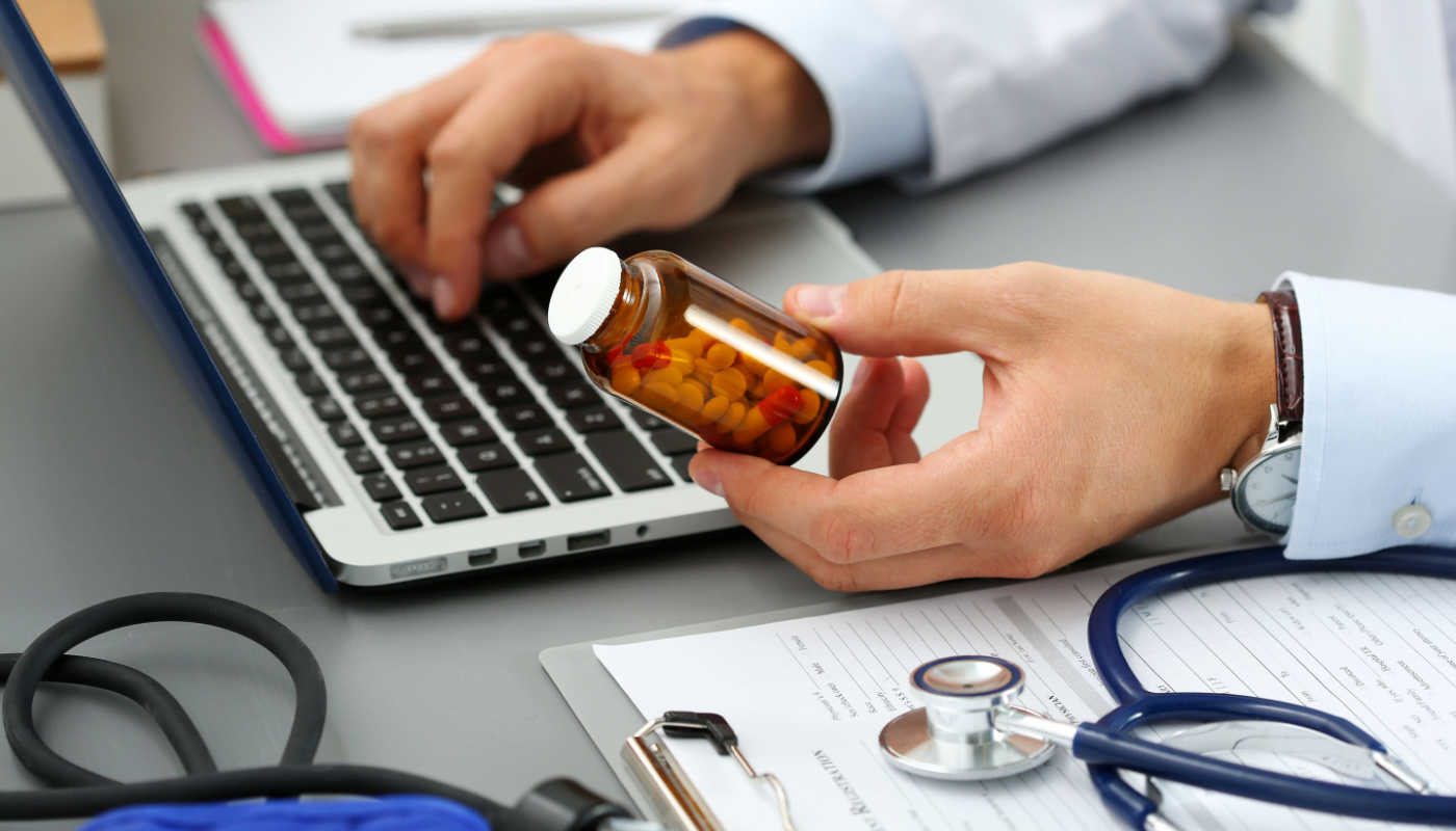 Pharmacist holding bottle of pills, inputting information into laptop; Specialty Pharma KPIs concept