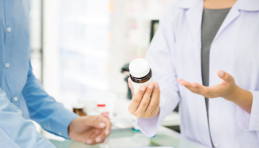 Pharmacist holding bottle of medication and talking to patient; biosimilars concept