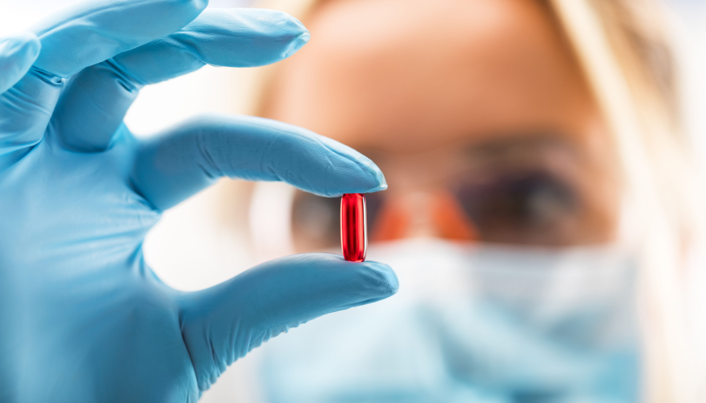 Scientist holding a red transparent pill in a pharmaceutical research laboratory; pharma market insights concept
